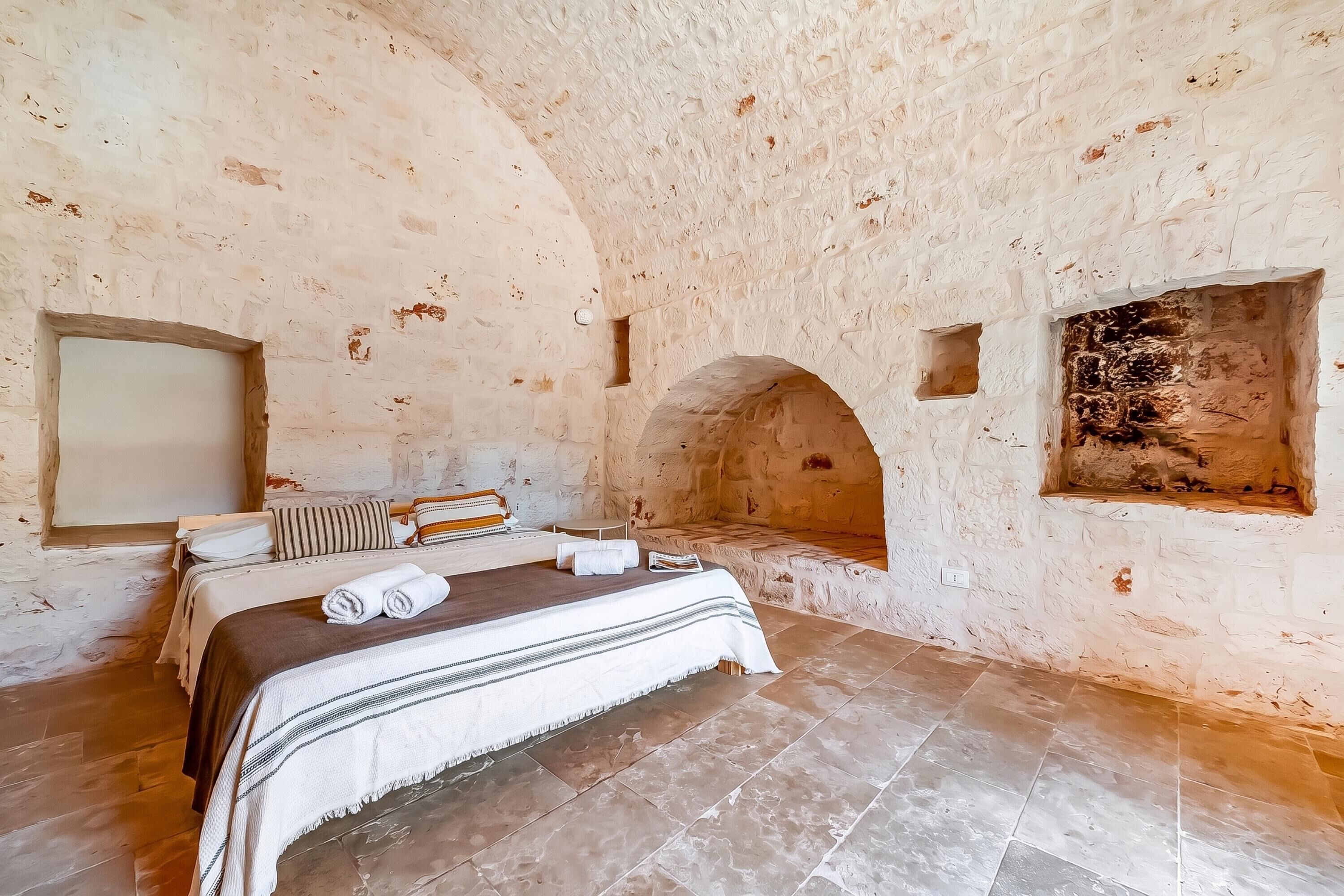 A rustic room with a bed, a small seating area, and a stone wall.