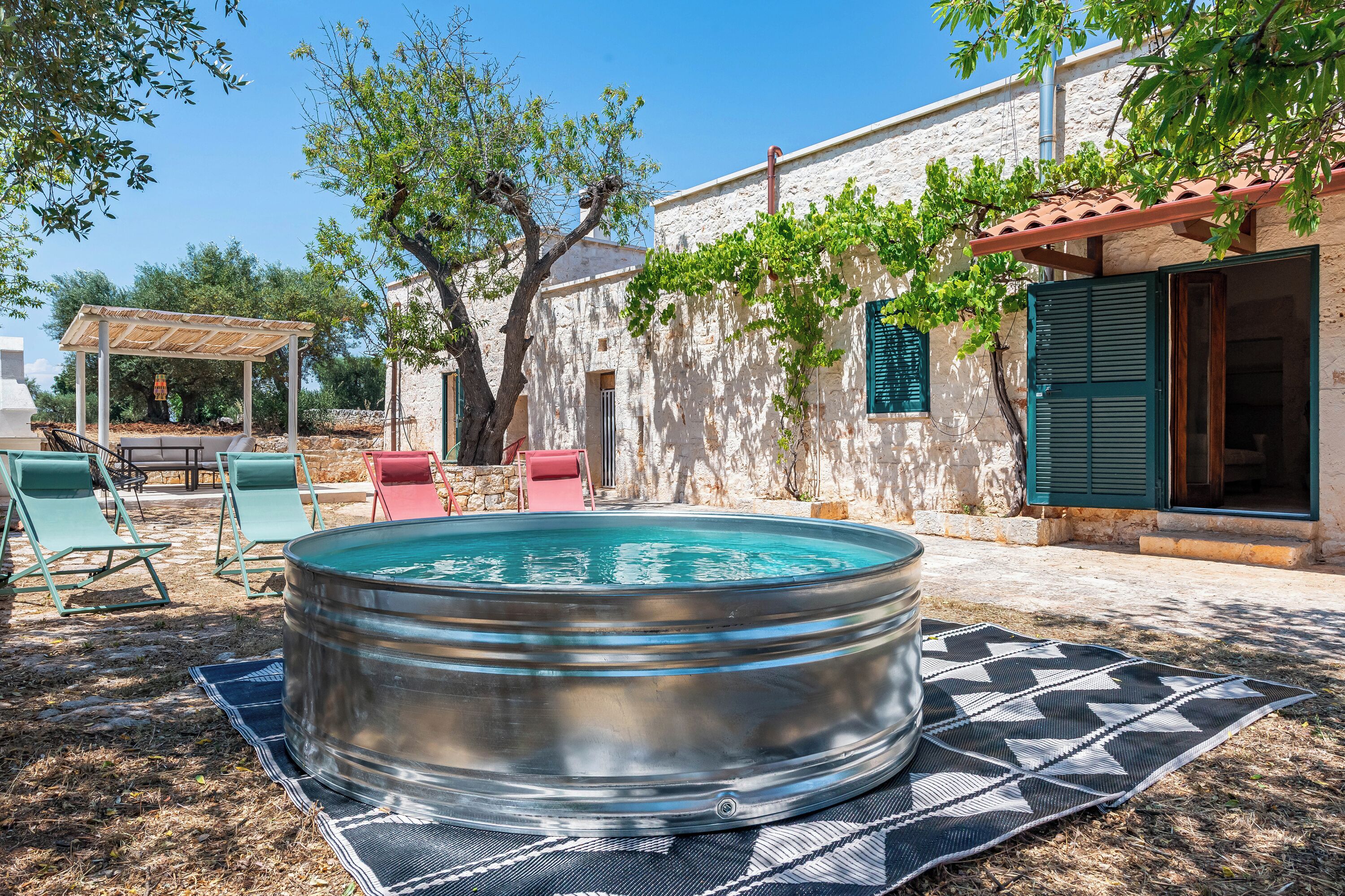 A hot tub in a backyard with a pergola, outdoor seating, and a stone wall.
