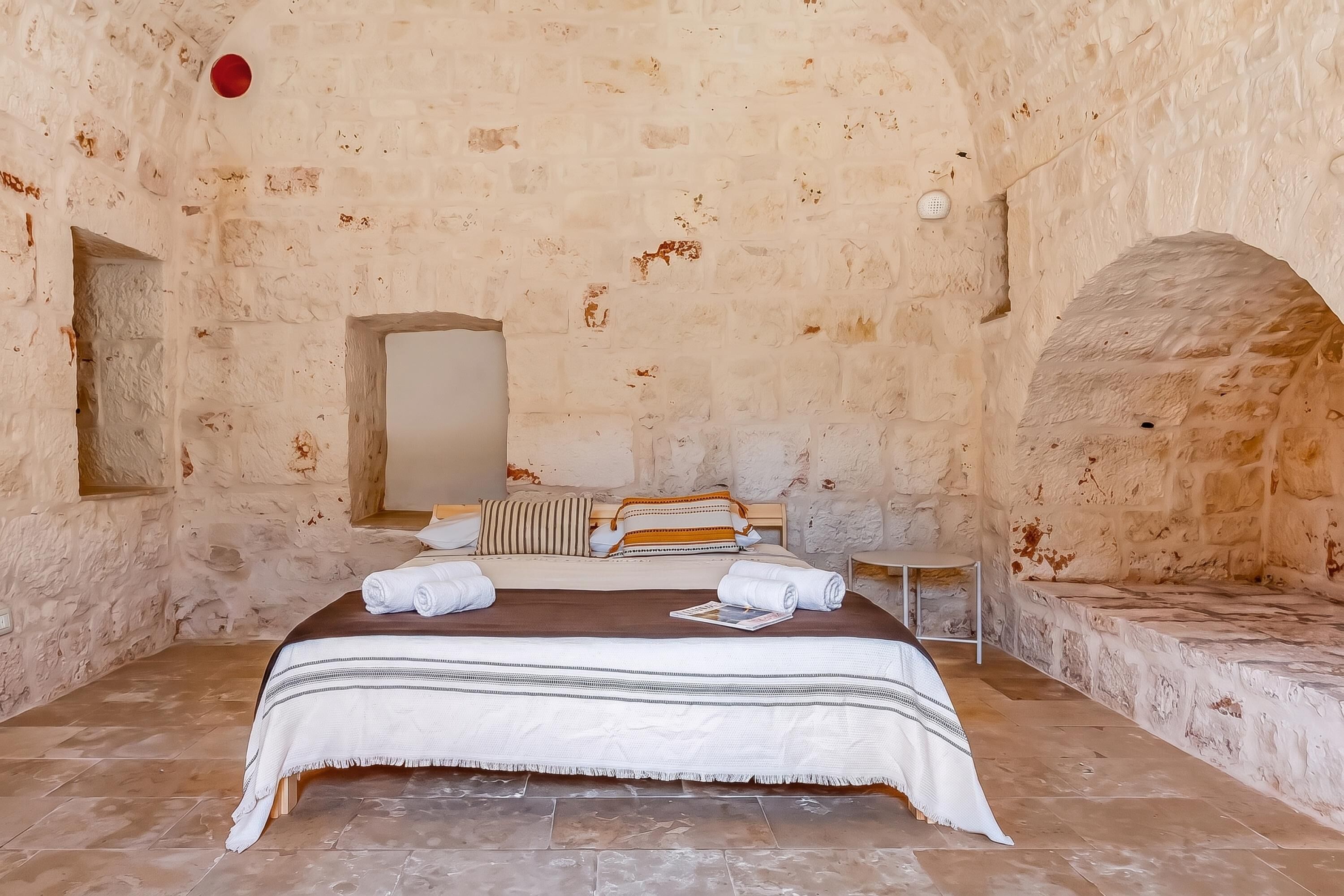 A stone-walled room with a bed, a small table, and a bench.
