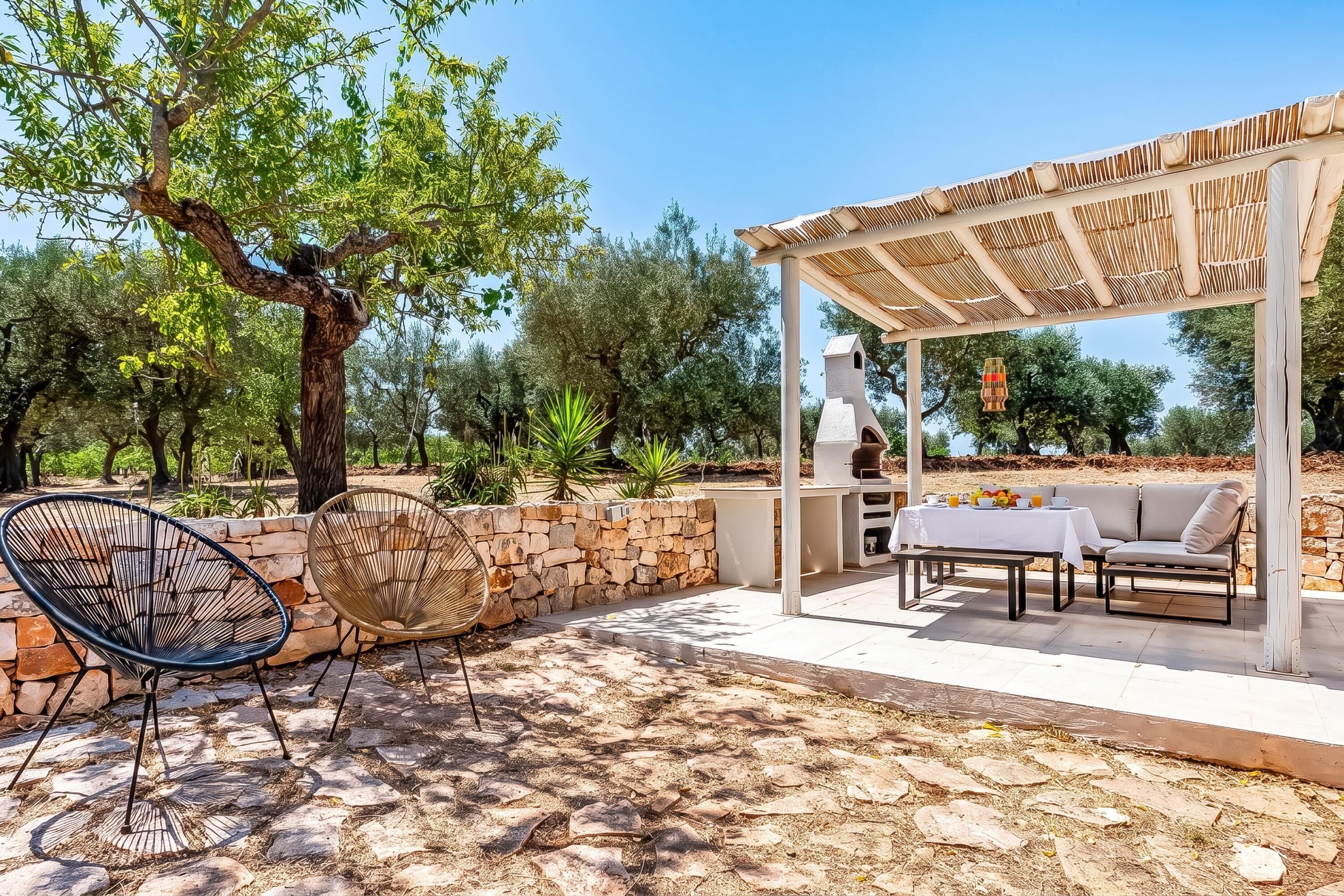 Un patio al aire libre con suelo de piedra, una pérgola, zona de barbacoa y mobiliario para sentarse.
