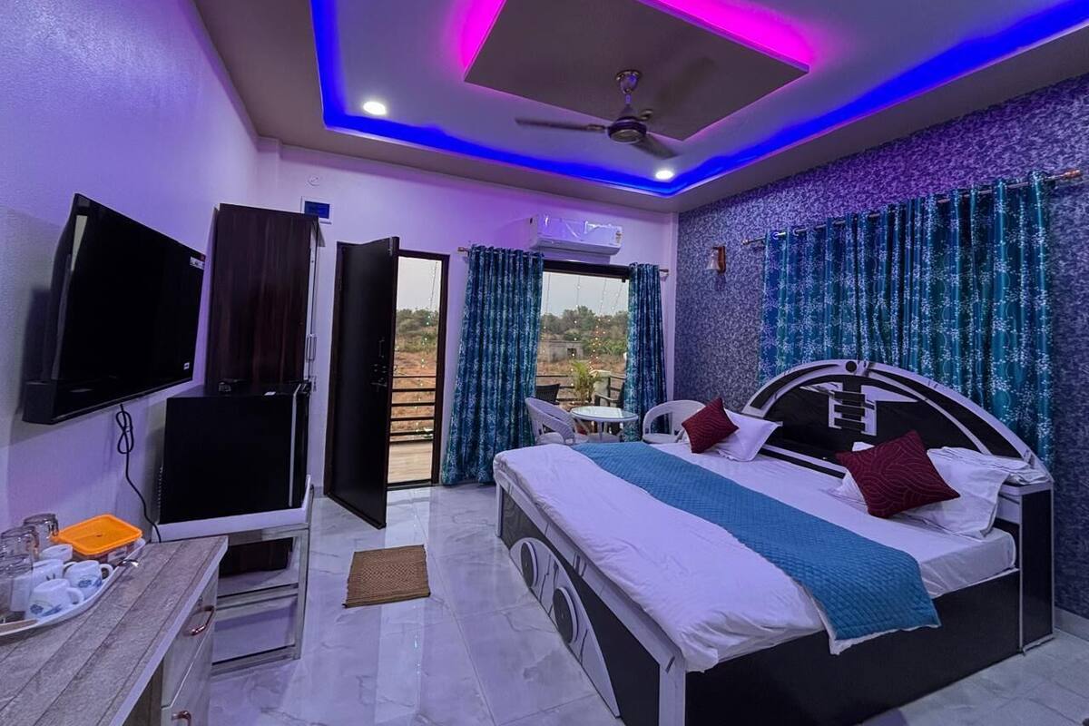 A modern bedroom with a bed, a TV, a desk, and a balcony with curtains.