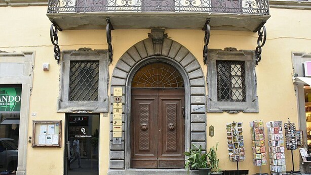 Un edificio con una puerta de madera grande, dos ventanas con rejas metálicas y un balcón con ornamentos de hierro.