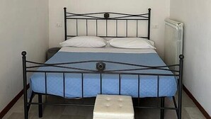 Un dormitorio pequeño y ordenado con una cama individual, una mesita de noche y un taburete.