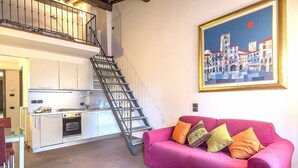 Una cucina moderna con una scala che conduce a un livello superiore, un divano rosa con cuscini e un quadro appeso al muro.