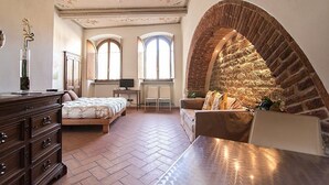 A spacious room with a large bed, a wooden dresser, a seating area with a sofa, and a stone fireplace. - Appartamento Vasaria B: A graceful studio apartment located in the historic center of Arezzo, with Free WI-FI. (Arezzo)
