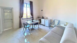 A compact living space with a dining table, a sofa, a kitchenette, and a window with curtains.