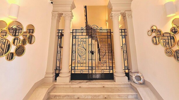 A grand entrance with a decorative metal gate, white columns, and wall sconces with circular mirrors.