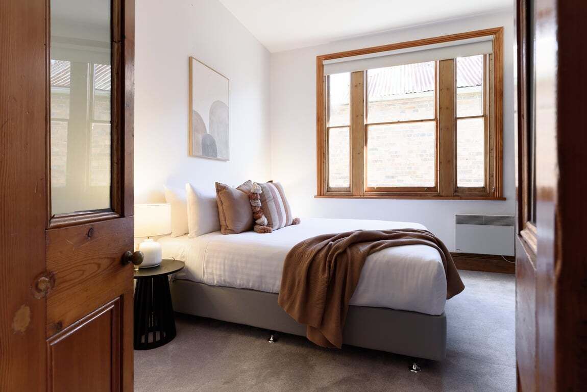 A bedroom with a bed, a bedside table, a lamp, a window, and a wall-mounted picture.
