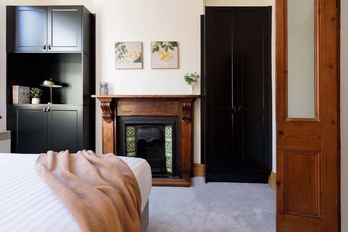 Une chambre à coucher avec un lit, une cheminée, une armoire et deux tableaux encadrés accrochés au mur.