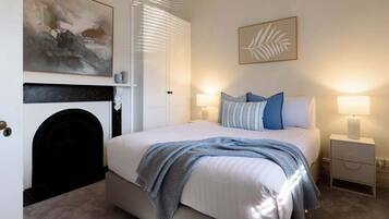 A bedroom with a bed, bedside lamps, a fireplace, and artwork on the walls.