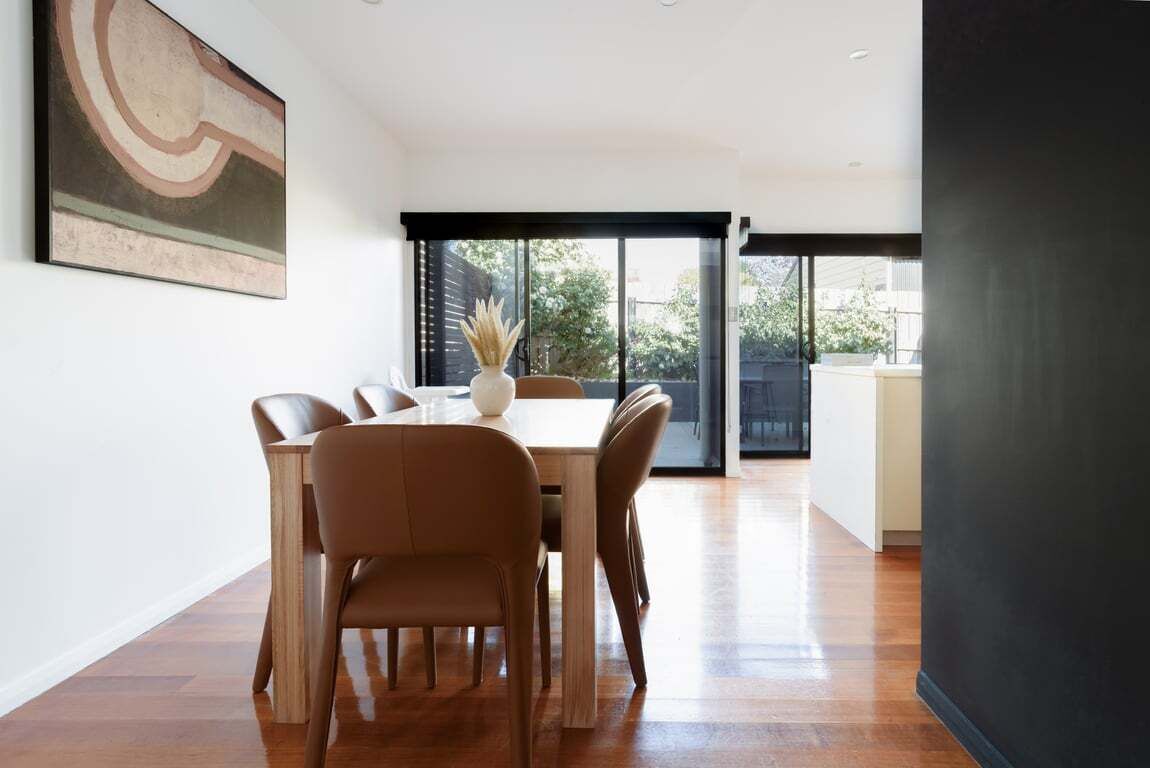 A modern dining area with a wooden table and chairs, a vase with dried plants, and a large abstract painting on the wall.