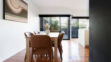 A modern dining area with a wooden table and chairs, a vase with dried plants, and a large abstract painting on the wall.