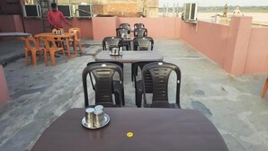 A rooftop dining area with tables and chairs, a person in the background, and a view of a temple in the distance. - Sankatha Guest House (Varanasi)