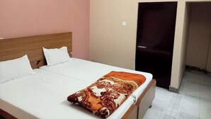 A hotel room with a bed, a headboard, a door, and a wall socket. - Sankatha Guest House (Varanasi)