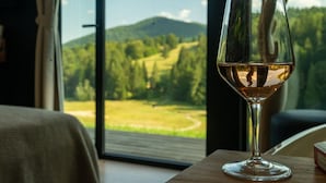 A glass of white wine on a table by a window with a view of a green landscape and mountains. - The Valley Resort (Vama Buzăului)