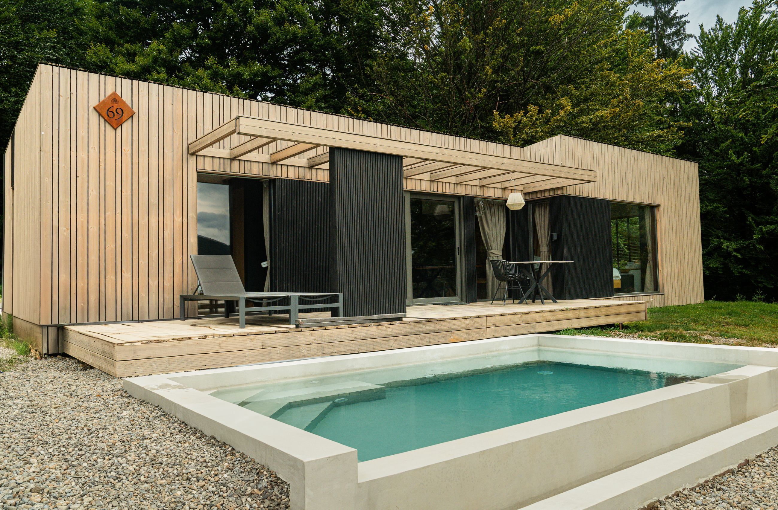 Un área de piscina moderna al aire libre con terraza de madera y una silla de descanso.