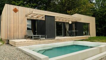 Un área de piscina moderna al aire libre con terraza de madera y una silla de descanso.