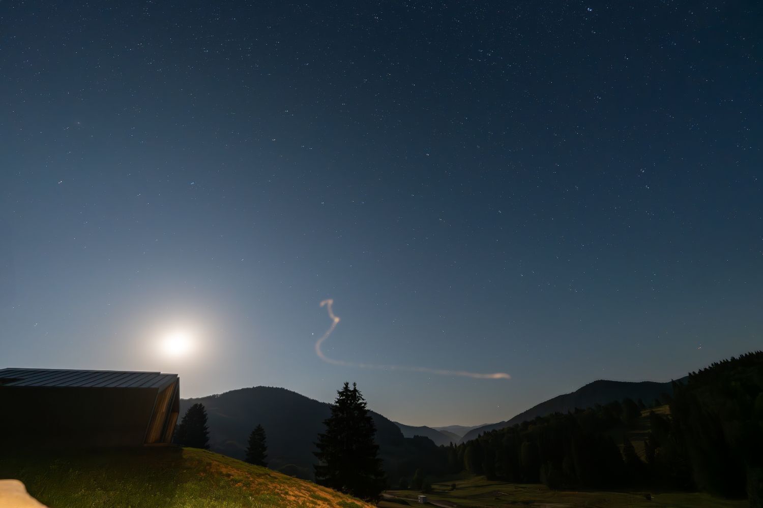 Ein Sternenhimmel mit sichelförmigem Mond und einem Kondensstreifen.