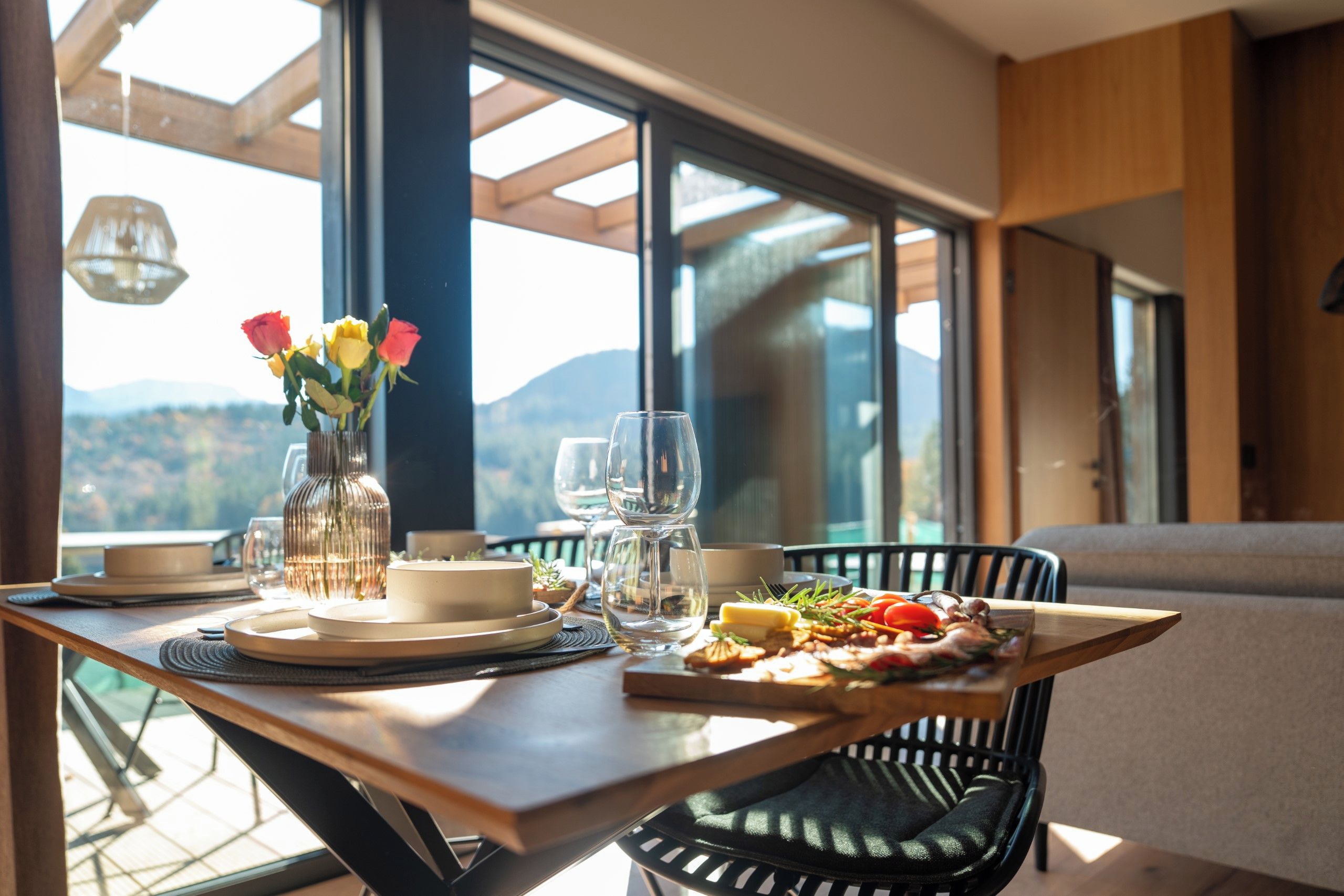 Une table à manger avec un repas, un vase rempli de fleurs et une vue sur l’extérieur.