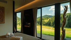 A bedroom with a large window, a bed with rolled towels, and a view of a green landscape. - The Valley Resort (Vama Buzăului)
