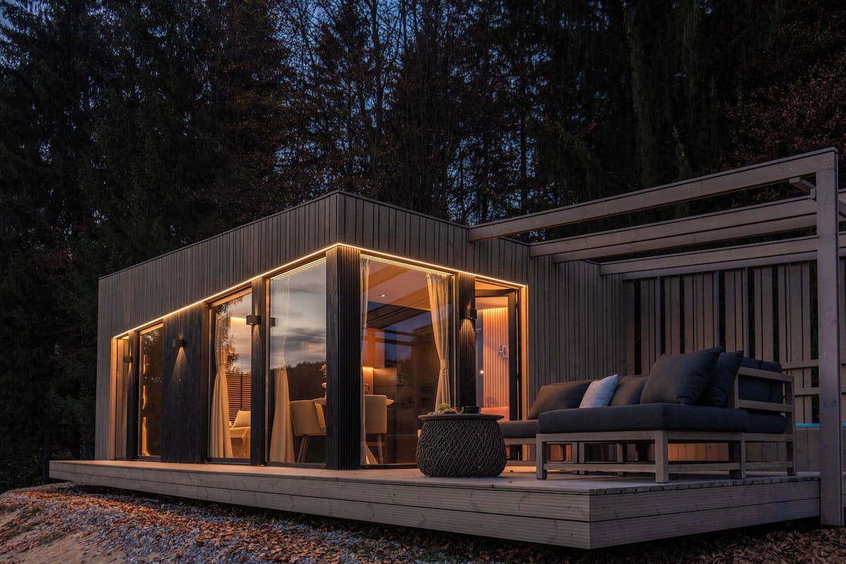 A modern cabin with a glass-enclosed living area, a wooden deck, and a cozy seating area.