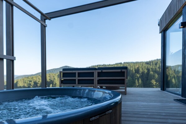 A hot tub on a wooden deck with a view of a forested mountain range. - The Valley Resort (Vama Buzăului)