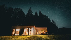 A cabin with a large open window, a wooden exterior, and a view of the night sky. - The Valley Resort (Vama Buzăului)
