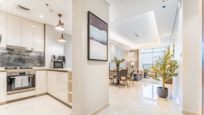 A modern kitchen with built-in appliances, a dining area with a large table and chairs, and a potted plant. - Spacious High-Floor 2BR with Stunning City and Burj Khalifa Views (Dubai)