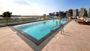A rooftop pool with a city view, lounge chairs, and a clear sky. - Spacious High-Floor 2BR with Stunning City and Burj Khalifa Views (Dubai)