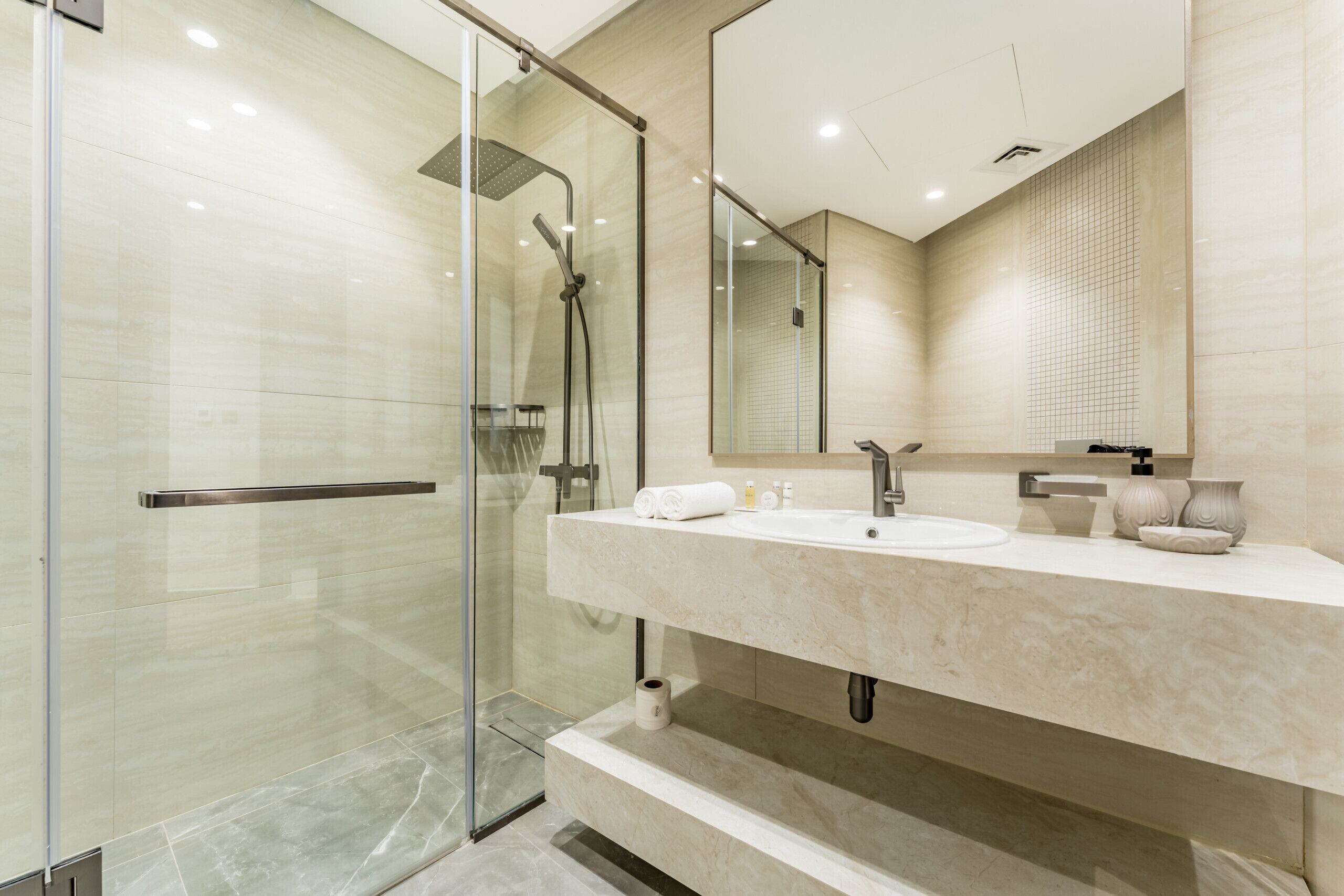 Une salle de bain moderne avec une douche à l’italienne en verre, un grand miroir et un plan de toilette en marbre.