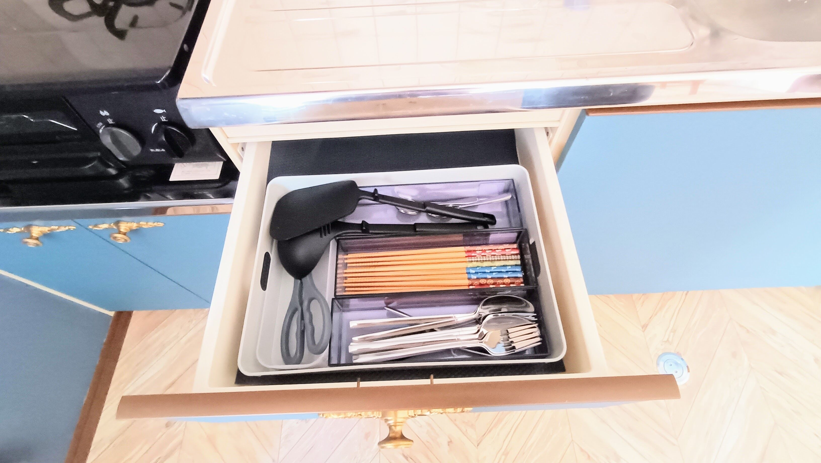 A drawer containing kitchen utensils, including a spatula, tongs, and a set of knives.