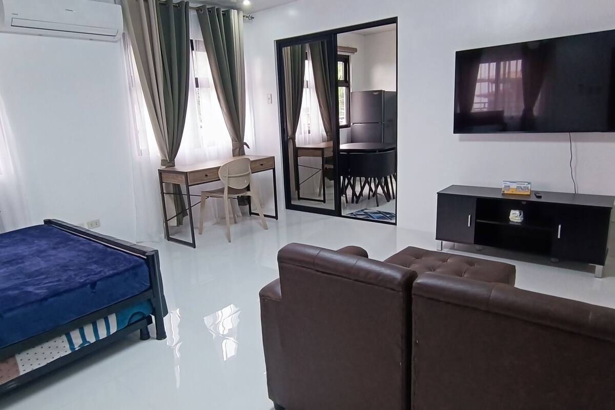 A hotel room with a bed, a sofa, a desk with a chair, a TV, and a mirror.