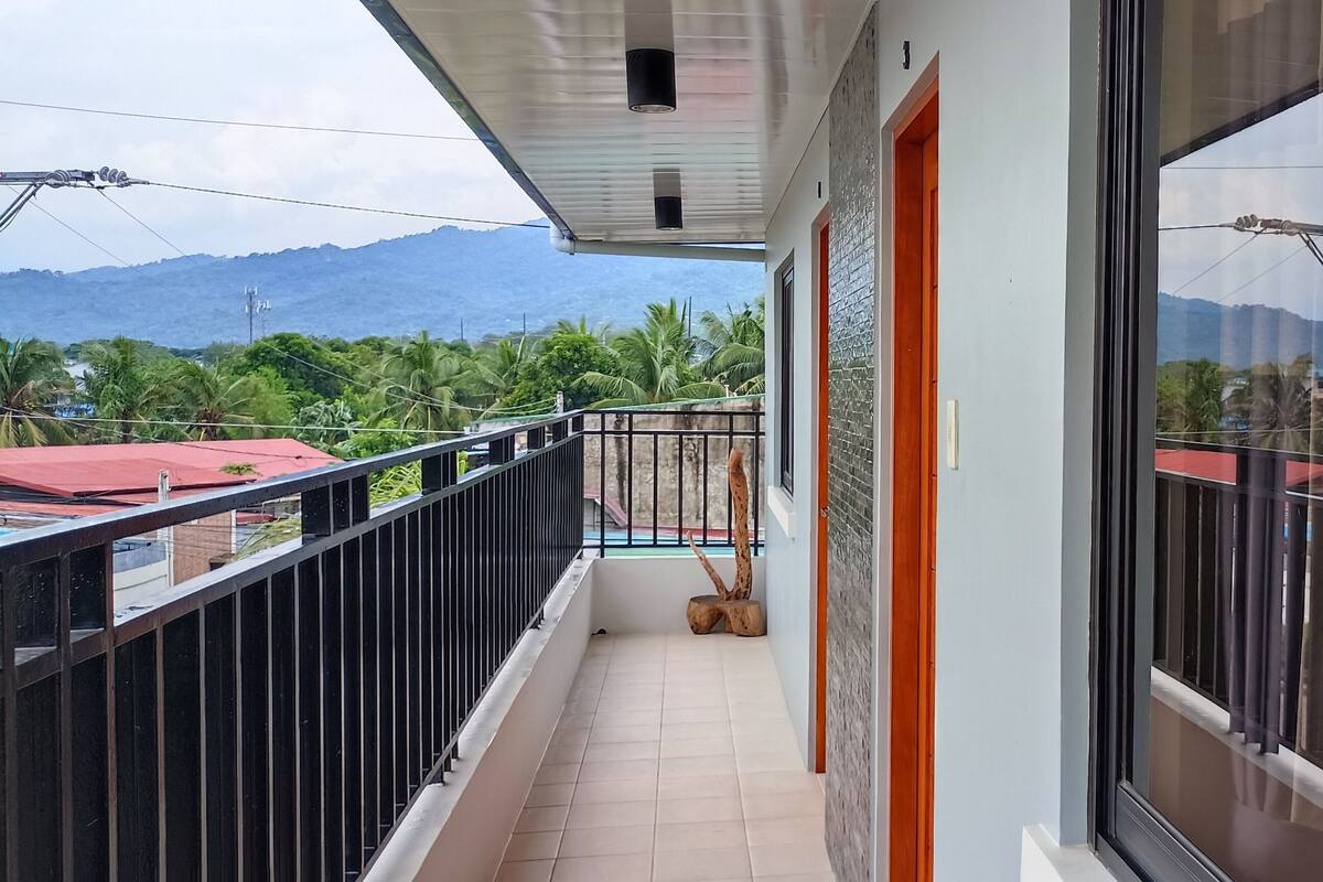 A balcony with a view of mountains and palm trees, a tiled floor, and a wooden tree trunk.