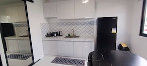 A compact kitchen with white cabinets, a black refrigerator, a sink, and a countertop with a coffee maker and kettle. - Stay at Diez (Calamba)