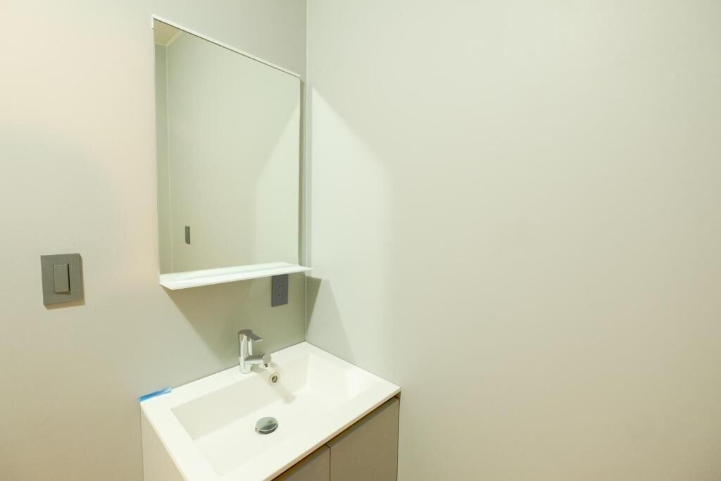 Un bagno con un lavandino bianco, uno specchio e un interruttore a muro.