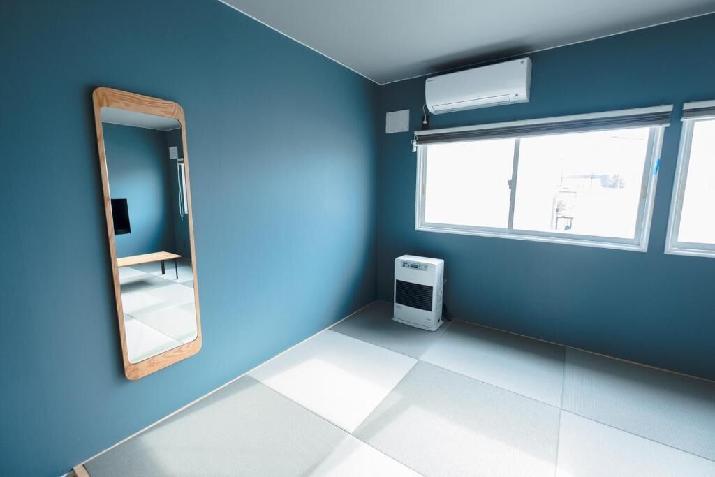 A room with teal walls, a large mirror, a window with blinds, and a portable air conditioner.