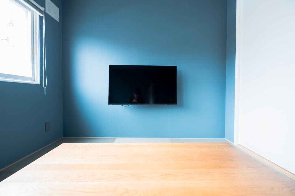 A room with a blue wall, a mounted television, and a wooden floor.