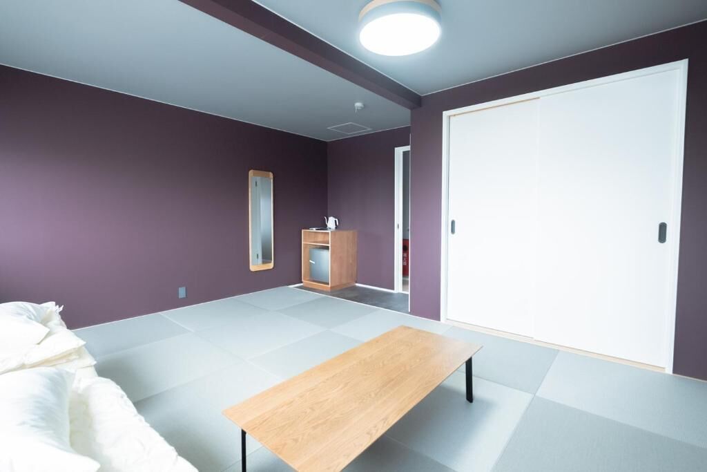 A room with a bed, a wooden table, a wardrobe, and a mirror.
