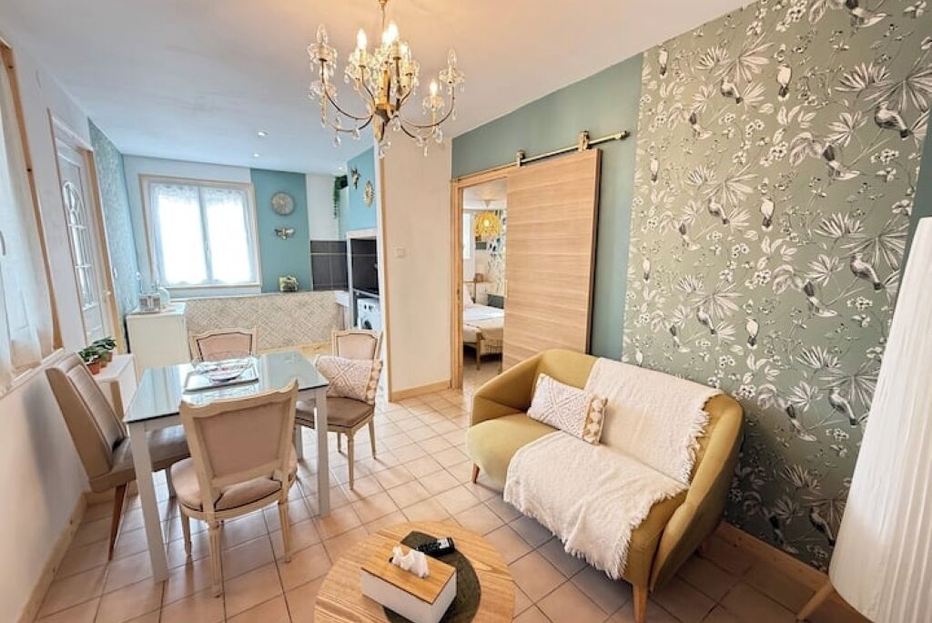 En hyggelig stue med sofa, spisebord med stole, lysekrone og blomstret tapet.