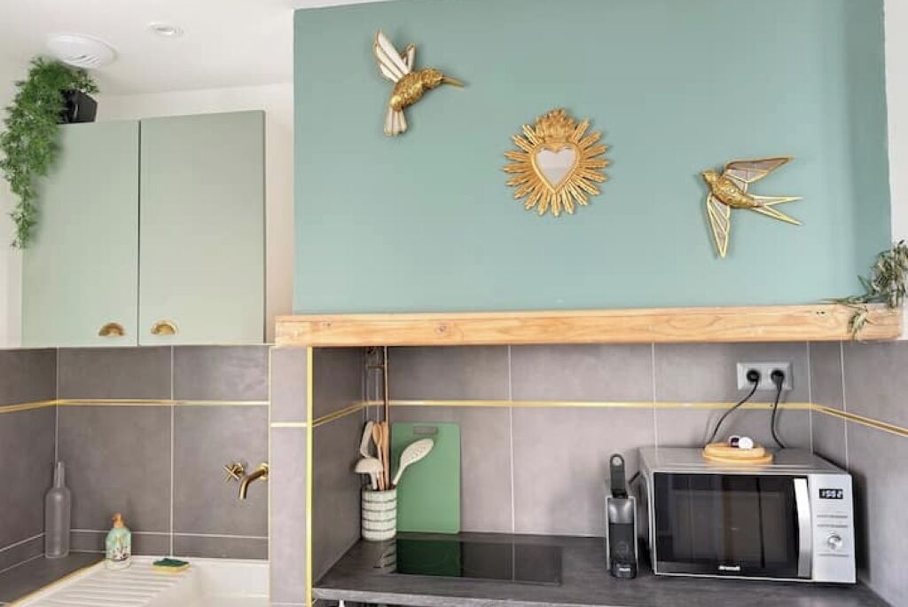 A kitchen with grey tiles, a microwave, a toaster, and a green cutting board.