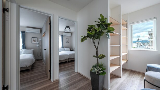 Habitación de hotel moderna con piso de madera, una planta grande en maceta, vista por la ventana y un mueble de almacenamiento empotrado.