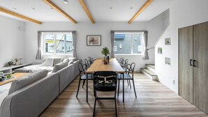 Una sala de estar moderna con un sofá, una mesa de comedor y sillas. Se ve una escalera que sube a un nivel superior.