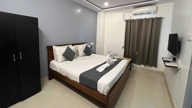 A neatly arranged bedroom with a bed, a wardrobe, a television, and a window with curtains. - White Ridge Hotel - Nagole (Hyderabad)