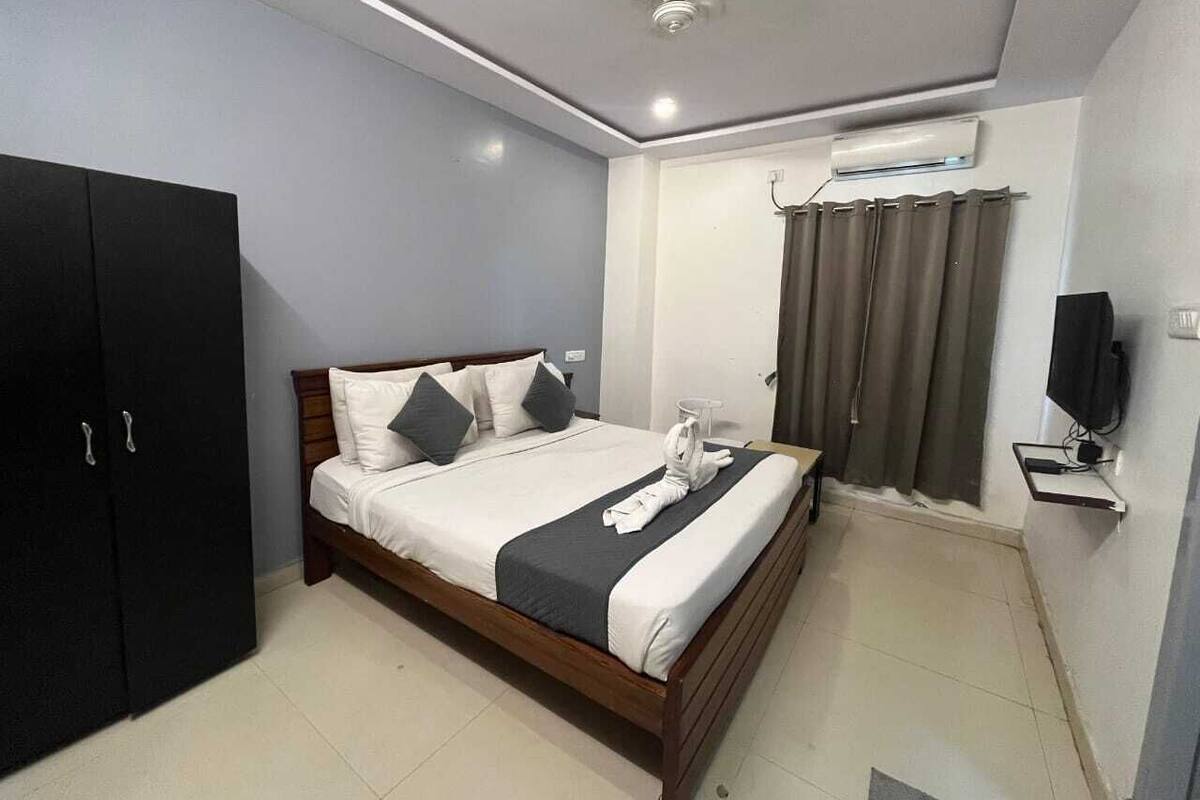 A neatly arranged bedroom with a bed, a wardrobe, a television, and a window with curtains.