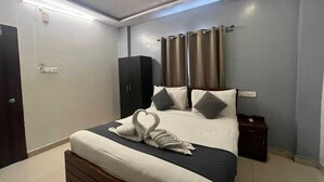 A neatly made bed with a heart-shaped towel arrangement, a dark headboard, and a bedside table with a lamp. - White Ridge Hotel - Nagole (Hyderabad)