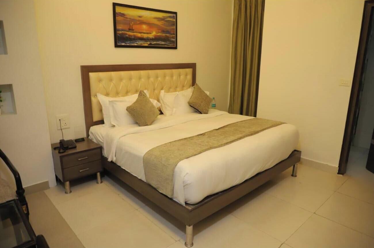 A neatly made bed with a wooden headboard, a bedside table with a phone, and a painting above the bed.