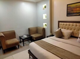 Una habitación de hotel con una cama grande, dos sillones, una mesita y un cuadro en la pared.