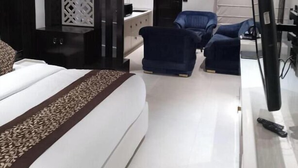 A modern hotel room with a large bed, a desk, two chairs, a TV, and an air conditioning unit. - Green Castle (Panipat)