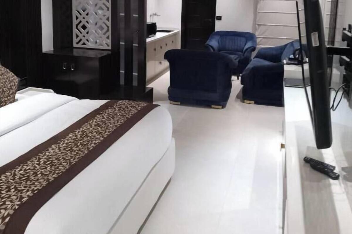A modern hotel room with a large bed, a desk, two chairs, a TV, and an air conditioning unit.