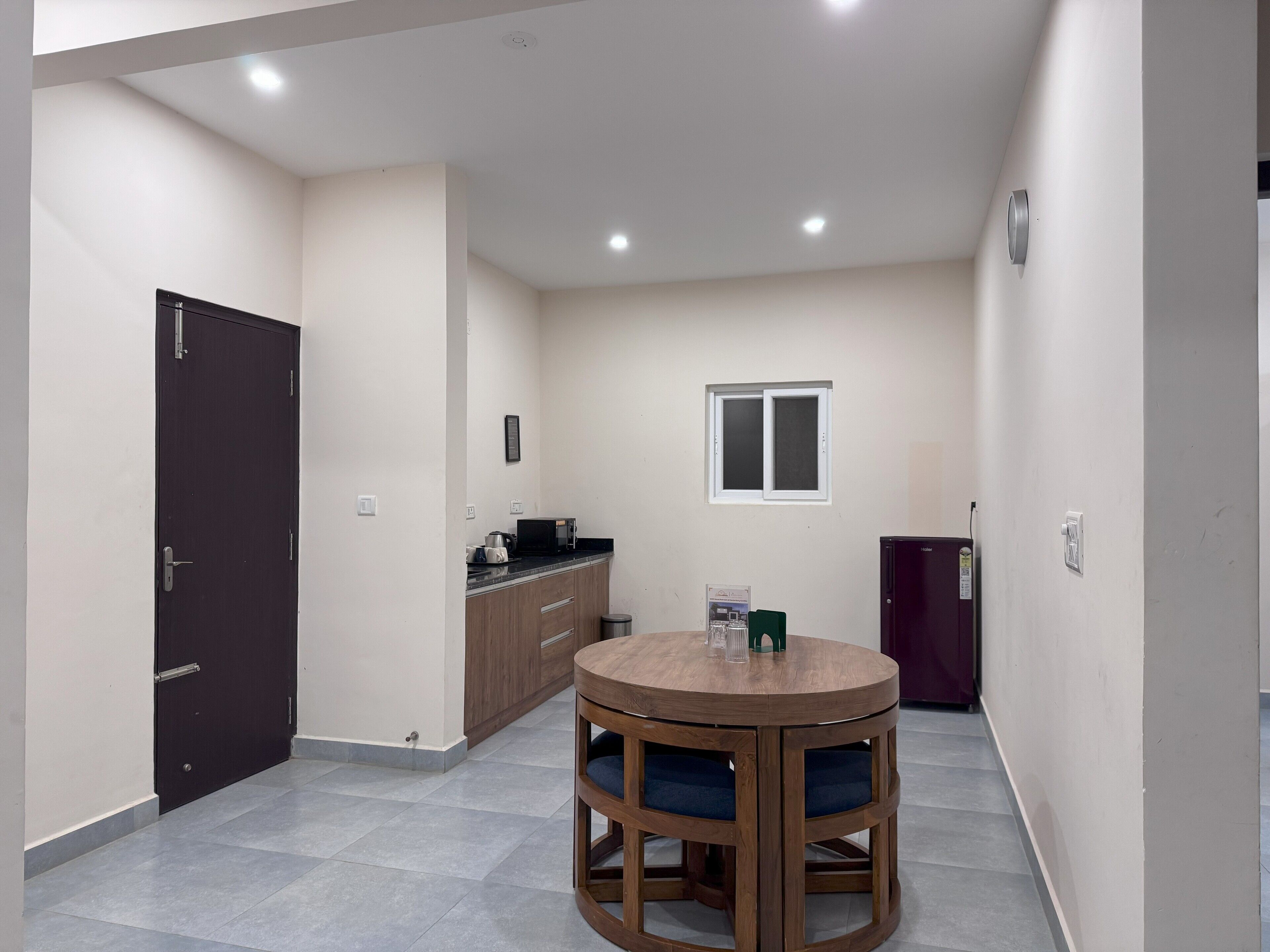 A compact kitchen with a dark door, a small window, and a round wooden table with blue cushions.